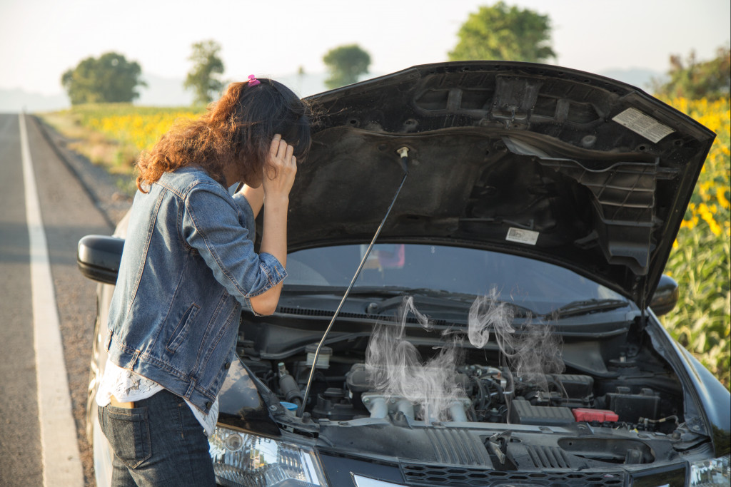 A woman looking at the smoking engine of her car beside the road