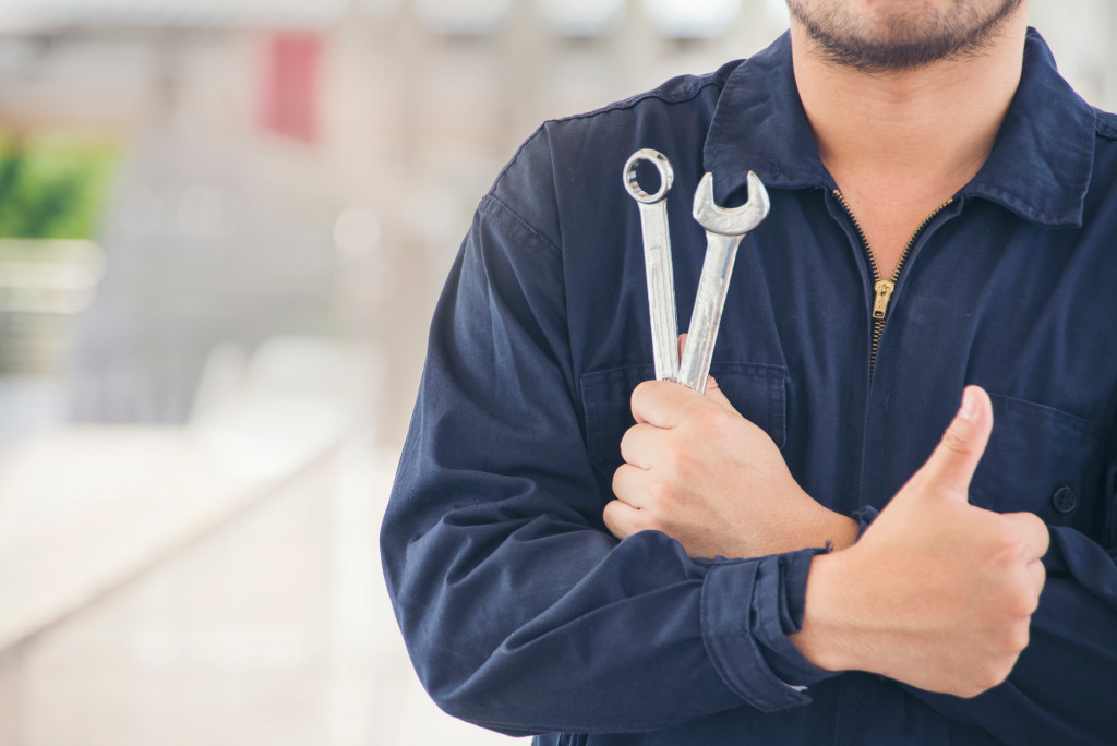 A mechanic holding tools in his hand and giving a thumbs-up as well